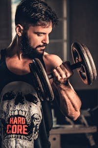 Bearded man in gym lifting a heavy dumbbell, showcasing strength and fitness.